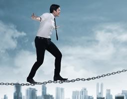 5 ways email meets B2B marketing challenges 5 A man in a shirt, tie and suit pants walks a tightrope made of metal chain links, with a city skyline in the background.