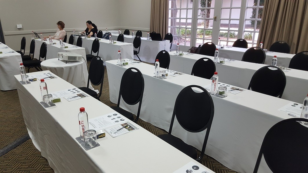 Lecture Room A room set up for a lecture with four rows of black chairs and tables covered in white cloths; the chairs are mostly empty.