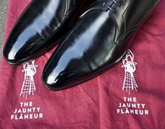 Eliminating Homelessness, One Shine at a Time… 2 A close-up shot of the toes of a pair of black dress shoes on a cloth that has "The Jaunty Flaneur" printed onto it twice.