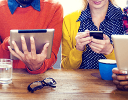 Rocketseed Launch Brand New User Interface... 12 7 people sit in a row at a table, each wearing colourful clothing and holding a tablet or smartphone.