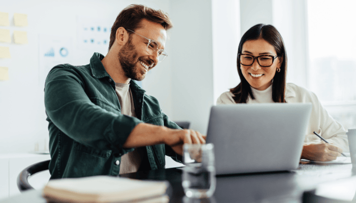 Debunking The Myth: SaaS Partner Programs Are Too Much Work 3 Two business people using a laptop together while sitting in a meeting. Happy business people reading myths about SaaS partner programs